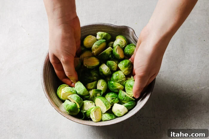 Caramelized Maple Bacon Brussels Sprouts 5 Hands tossing fresh halved Brussels sprouts in a bowl with olive oil, preparing for the recipe.