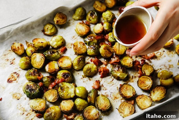 Caramelized Maple Bacon Brussels Sprouts 7 Hand pouring maple syrup over roasted Brussels sprouts and bacon on a baking sheet.