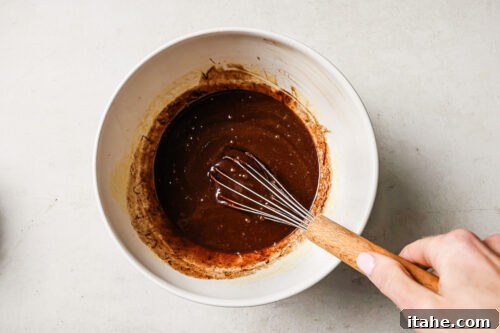 Rich pecan pie brownie batter in a white mixing bowl, ready to be poured into the pan for baking.