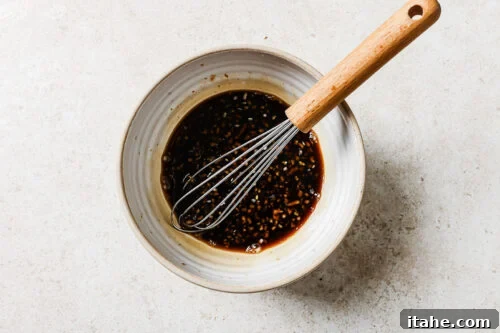 Homemade honey garlic sauce in a white bowl with a whisk, ready for glazing chicken.