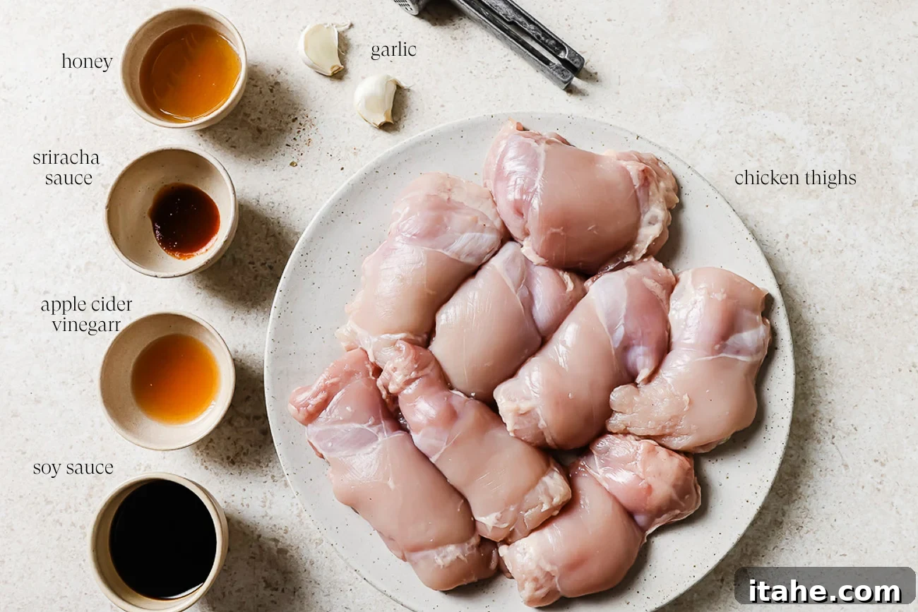 Sticky Honey Garlic Thighs 3 Raw chicken thighs on a plate, ready to make Honey Garlic Chicken Thighs, are surrounded by bowls of honey, sriracha sauce, apple cider vinegar, soy sauce, fresh garlic cloves, and measuring spoons on a light countertop.