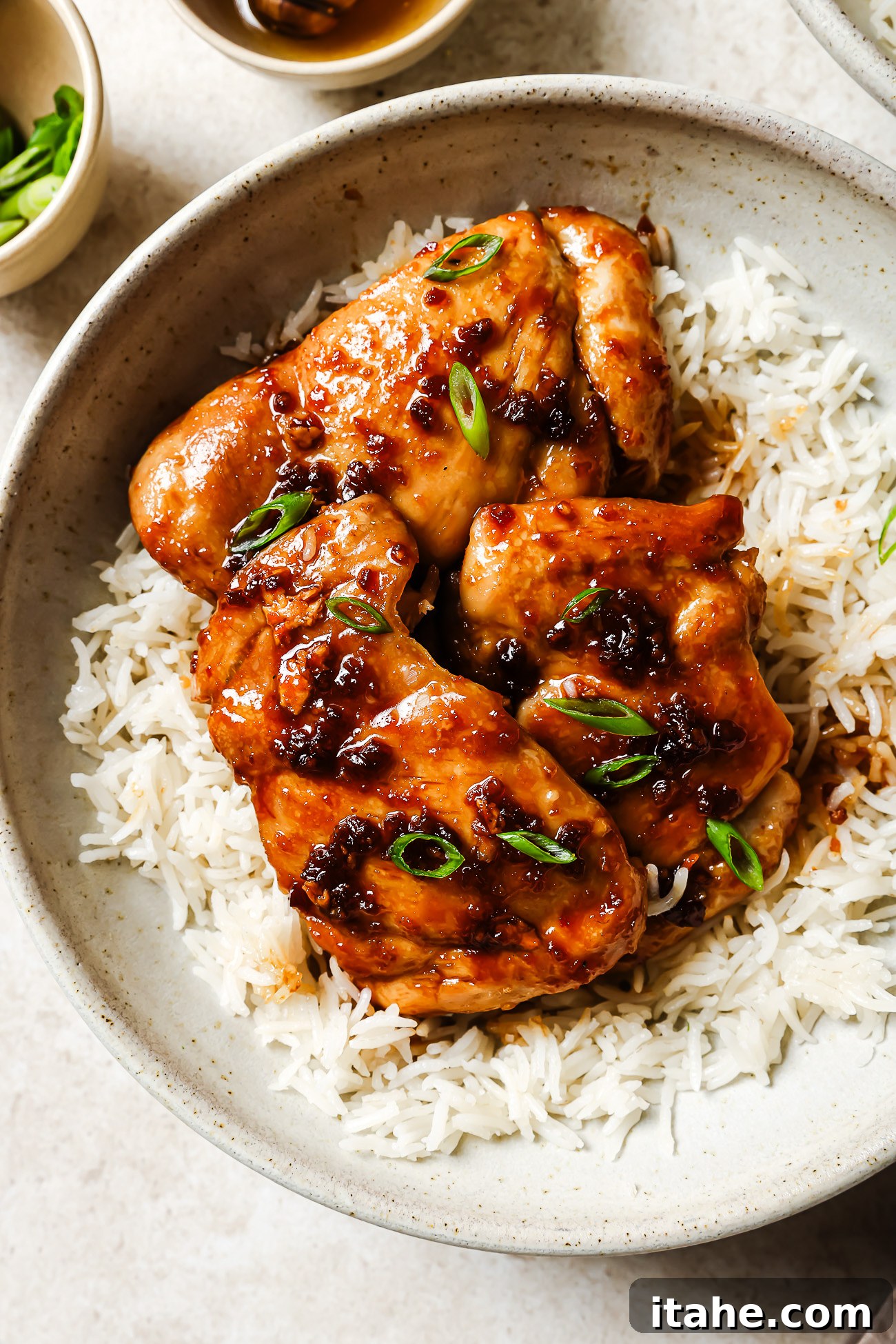 Sticky Honey Garlic Thighs 8 Close-up of honey garlic chicken thighs served over rice in a white bowl, garnished with green onions.