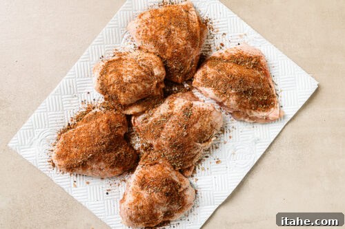 Seasoned raw chicken thighs arranged on a cutting board, ready for searing.