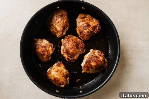 Chicken thighs sizzling in a hot skillet, achieving a golden-brown sear.