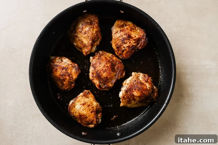 Cooked chicken thighs in a cast iron skillet, golden brown and sizzling.