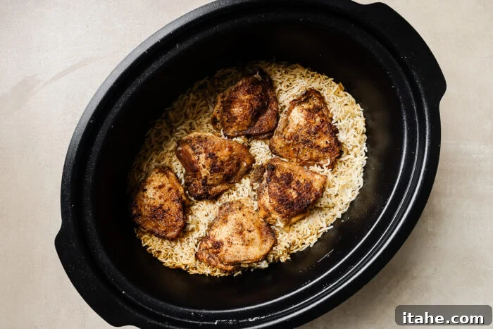 Overhead view of chicken and rice simmering inside a slow cooker pot with the lid partially open.