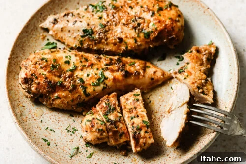 Slow cooker chicken breasts served on a plate with a fork.