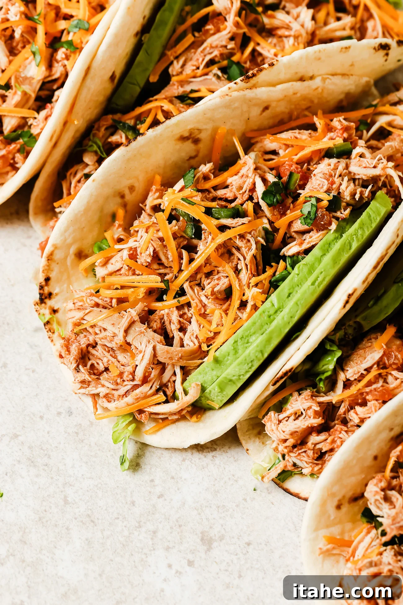 Close-up view of slow cooker chicken tacos filled with shredded chicken, salsa, and fresh toppings. 
