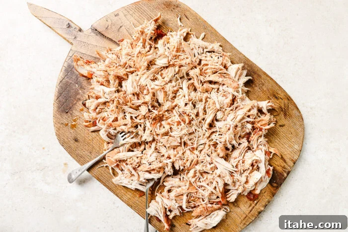Tender shredded chicken on a wooden cutting board.