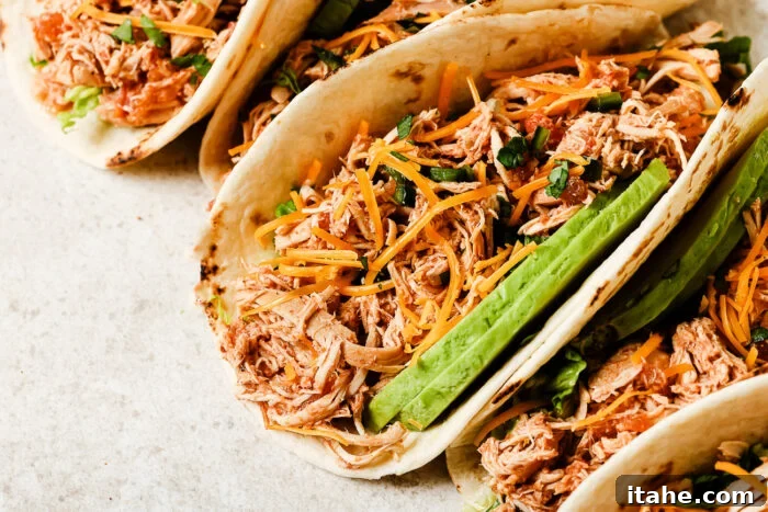Close-up view of slow cooker chicken tacos filled with shredded chicken, salsa, and fresh toppings.